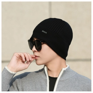 Detail of black ribbed knit beanie featuring a small silver metal logo plate on the cuff