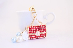 Detailed close-up of a golden mini handbag keychain with red rhinestones and white rose charm