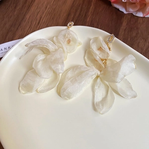 Detailed macro view of white chiffon flower earrings with rhinestones and metal accents