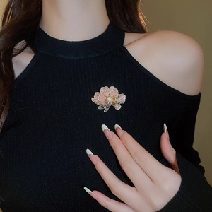 Detail of pink enamel flower brooch with white pearl on a black knitted sweater