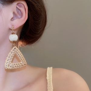 Detail of bohemian triangle straw woven earring with wooden beads and golden stud