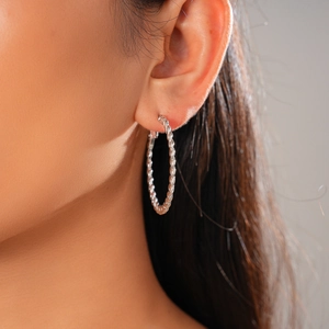 Detail view of a silver twisted rope hoop earring worn by a model for a stylish look