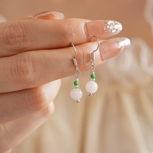 Detail view of pink and green bead earrings with silver hooks on soft beige background