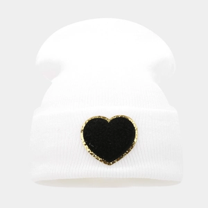 Detail of white ribbed beanie featuring a black heart patch with gold sequin border