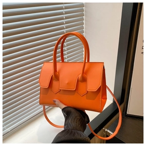 Detail of orange leather handbag with top handle and strap held by a model