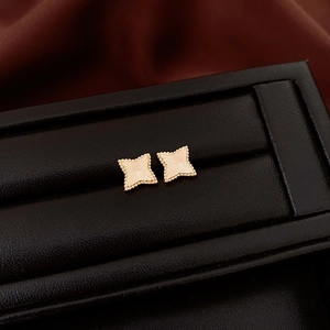 Macro shot of gold star stud earrings with radial texture on a black display stand