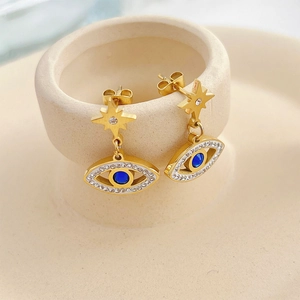 Gold star-shaped earrings with crystal-studded evil eye pendants on a ceramic dish