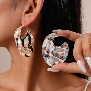 Boucles d'oreilles argentées irrégulières avec texture métallique ondulée sur modèle