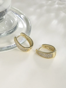 Detailed macro of gold U-shaped hoop earrings featuring four rows of white zircons
