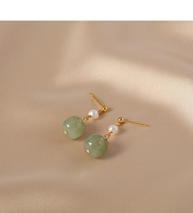 Close-up of vintage earrings featuring white pearls and green jade on champagne silk