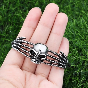 Macro shot of stainless steel skull bangle with skeleton hand design on green lawn