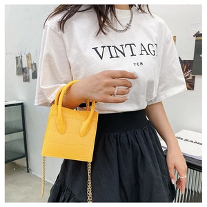 Detail view of yellow crocodile pattern handbag with top handle and gold chain strap