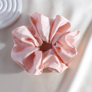 Close-up of pink satin silk scrunchie showing smooth texture and elegant folds