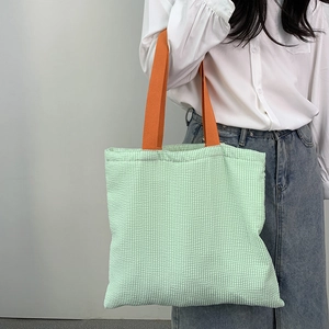 Detail of green and white striped canvas tote bag with vibrant orange handles