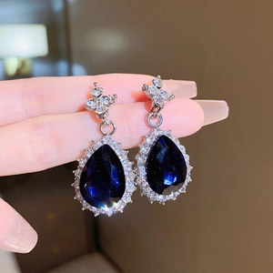 Macro shot of silver stud earrings with deep blue pear-cut gems and sparkling rhinestones