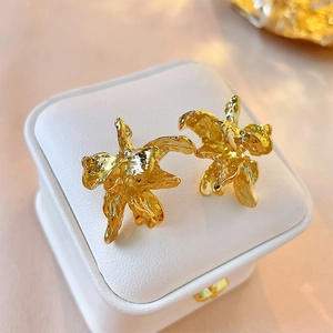 Irregular golden metal flower earrings with wrinkled petal design on white leather