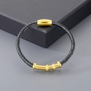 Detail of black woven leather bracelet with gold magnetic clasp and metal rings