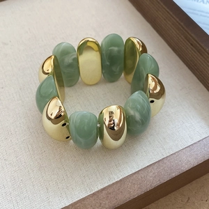 Detail of chunky gold metal beads and sage green marbled resin beads on elastic bracelet