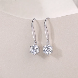Macro shot of silver drop earrings with round moissanite in a six-prong setting