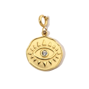 Macro detail of a golden coin pendant featuring evil eye relief and a white zircon stone