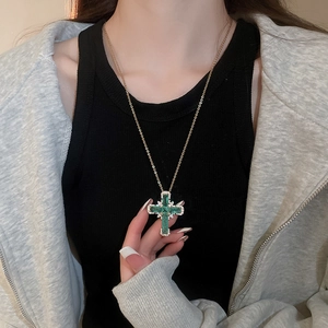 Détail d'un pendentif croix doré orné de pierres vert émeraude et d'accents diamantés