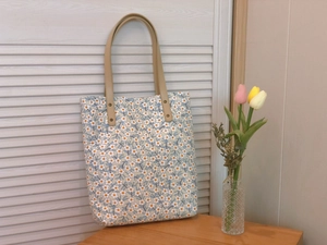 Détail du sac cabas en toile fleurie avec poignées en cuir marron et rivets métalliques