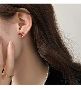 Detailed side view of high-gloss red enamel bow stud earrings on a fashion model