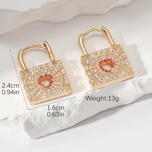 Golden heart lock earrings with red zircon stones on a white stone background