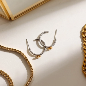 Detail von silbernen Creolen mit goldenem Herzanhänger auf minimalistischem Grund