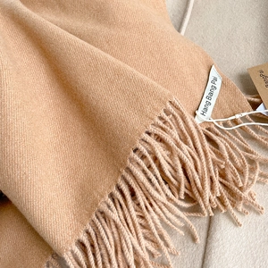 Dettaglio ravvicinato della trama in cashmere color cammello e delle eleganti frange