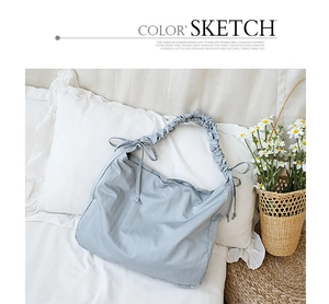 Close-up of light blue nylon shoulder bag featuring unique ruched strap on soft bedding