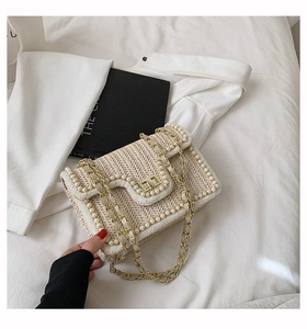 Detail of a straw crossbody bag with pearl trim, gold chain, and V-weave pattern