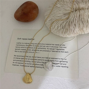 Macro detail of gold and silver shell pendants on sleek snake chains with coral decor