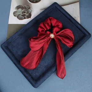 Close-up of red satin bow scrunchie with elegant pearl accent on blue velvet surface