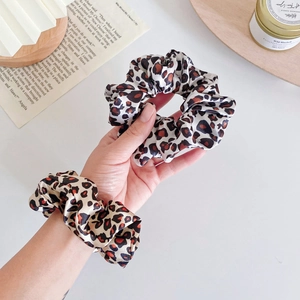 Close-up of leopard print silk scrunchies set worn on wrist with elegant lifestyle setup
