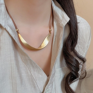 Detail of twisted gold metal pendant on dark brown cord necklace with elegant beads