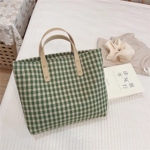 Detailed view of green plaid canvas tote bag with leather handles and gold rivet accents