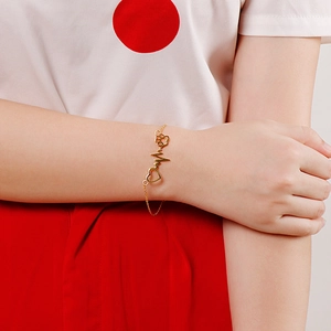 Detailed view of a gold heart and cat paw cutout bracelet on a model's wrist