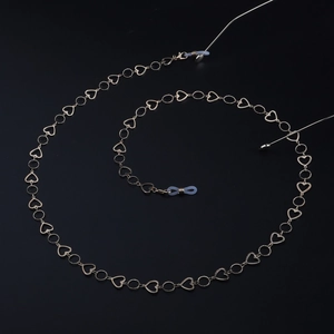Detail of golden heart-shaped eyewear chain with anti-slip silicone loops on black background