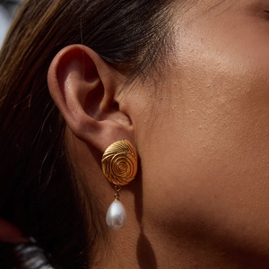 Detail of a gold spiral earring with a teardrop pearl pendant worn by a model