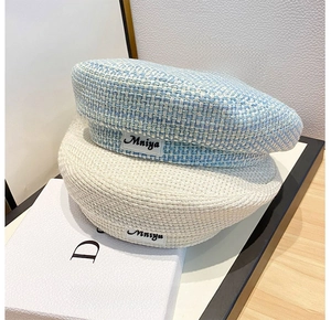 Detail of tweed and woven berets featuring Mniya logo labels in blue and beige