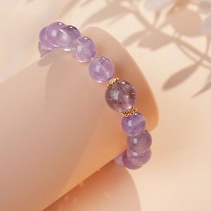 Detail of purple amethyst beaded bracelet featuring carved gold metal spacers on a stand