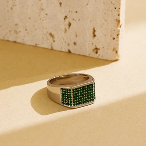 Macro shot of silver hip-hop ring with green pavé-set stones on travertine background