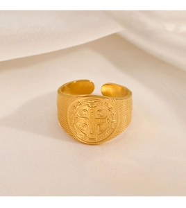 Macro detail of gold St. Benedict medal cross ring on white silk background texture