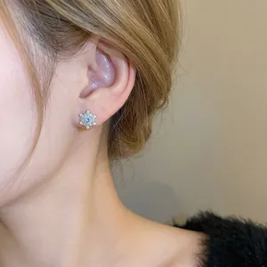Elegant silver snowflake stud earrings with light blue zircon worn on model's earlobe