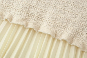 Détail du tissu en maille beige et de la jupe plissée jaune pâle montrant la texture
