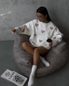 Close-up of oversized cream knit sweater with pink heart patterns in a cozy setting