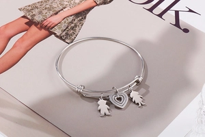 Detail of adjustable silver steel bracelet with boy, girl and heart charms on a magazine