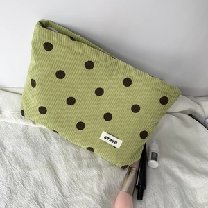 Macro view of green corduroy cosmetic bag with brown polka dots and brand label detail