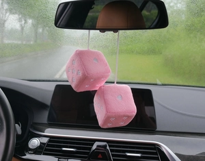 Close-up of pink plush car dice with white heart embroidery hanging on a rearview mirror